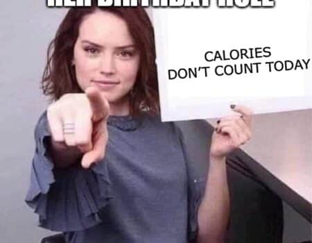 Woman pointing at a sign that says “Calories don’t count today” because it’s her birthday, proving she’s ready to eat cake without a single ounce of guilt.