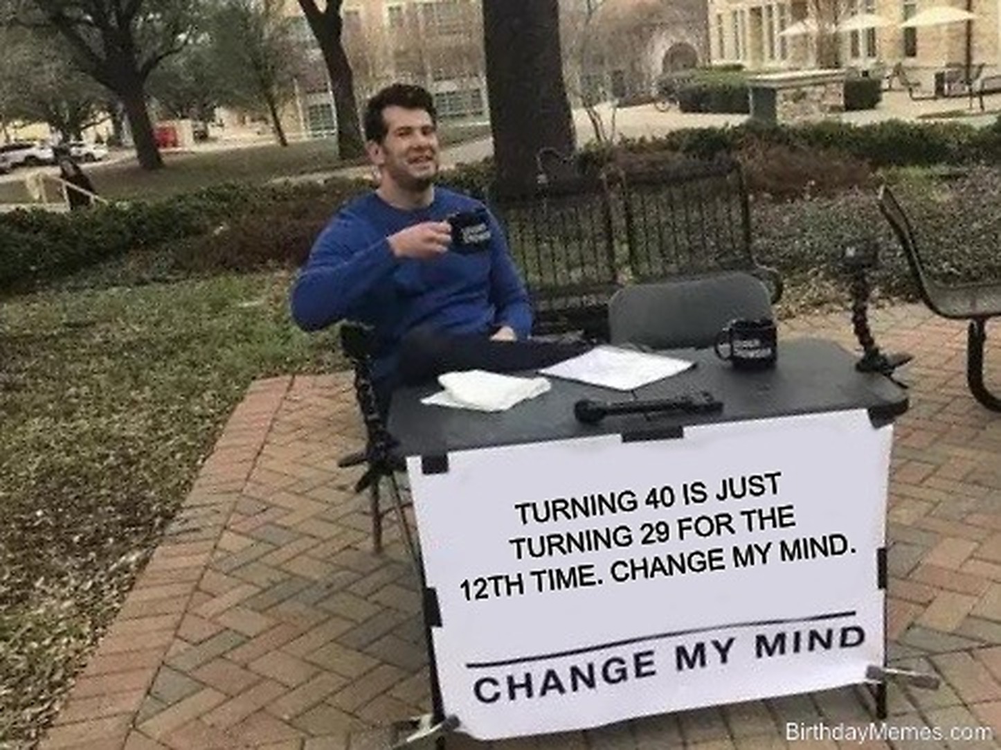 Man sitting at an outdoor table beside a sign reading: Turning 40 is just turning 29 for the 12th time. Change my mind.